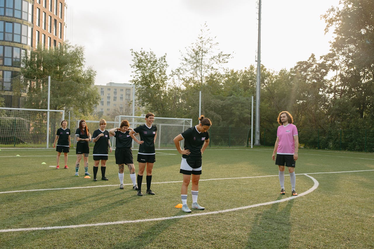 Womens soccer team practices drills on a sunny outdoor field with coach observing.