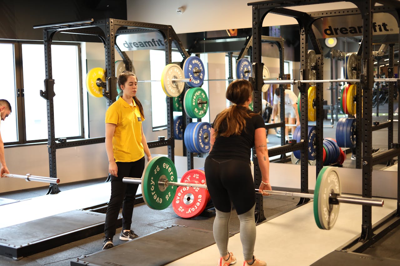 Two women weightlifting in a modern gym with colorful plates, showcasing fitness training.